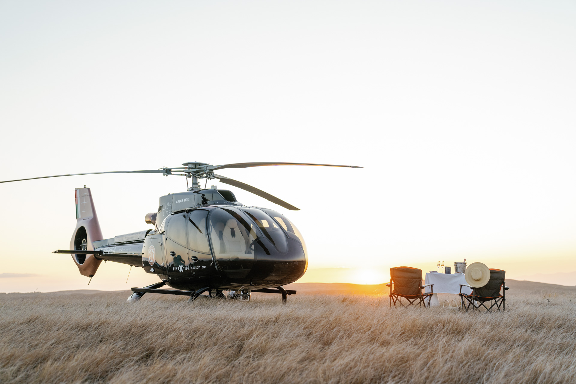 Private helicopter parked in tall grass at sunset