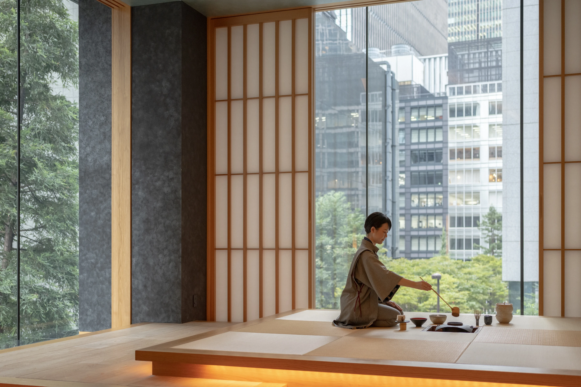 Traditional Japanese tea ceremony taking place in a serene tatami room with floor-to-ceiling windows overlooking a cityscape