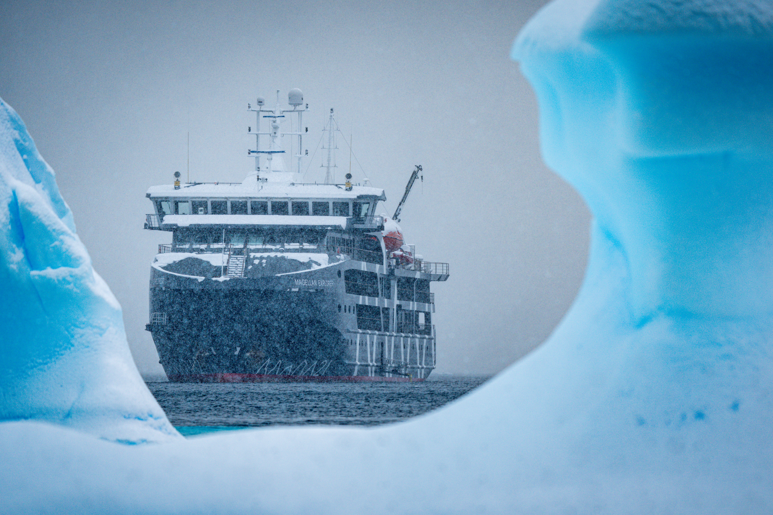 Antarctic expedition cruise ship navigating between icebergs in snowy conditions