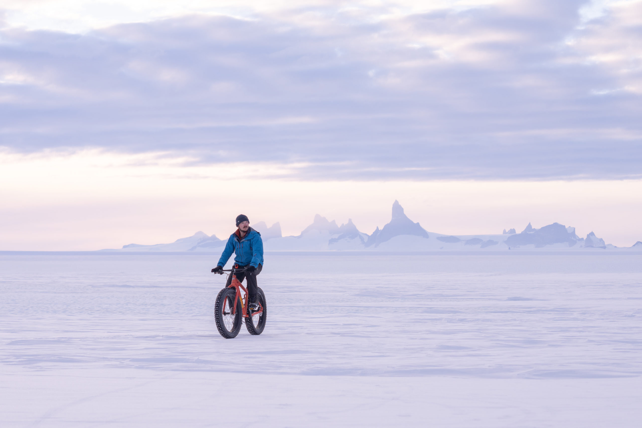 Traveler fat biking across a frozen Antarctic landscape with snow-covered mountains in the distance
