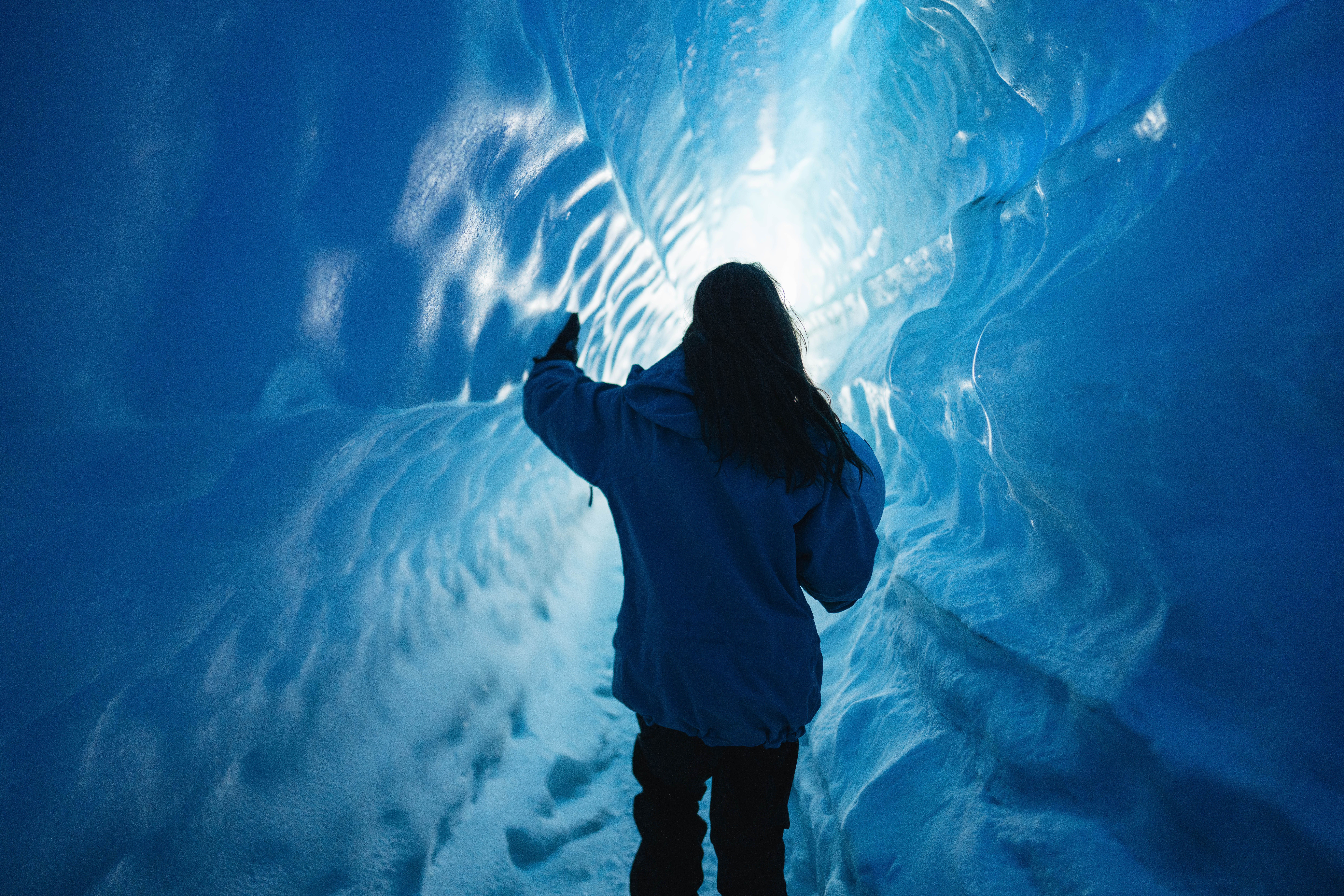 Traveler exploring a glowing blue ice cave in Antarctica, showcasing unique glacial formations