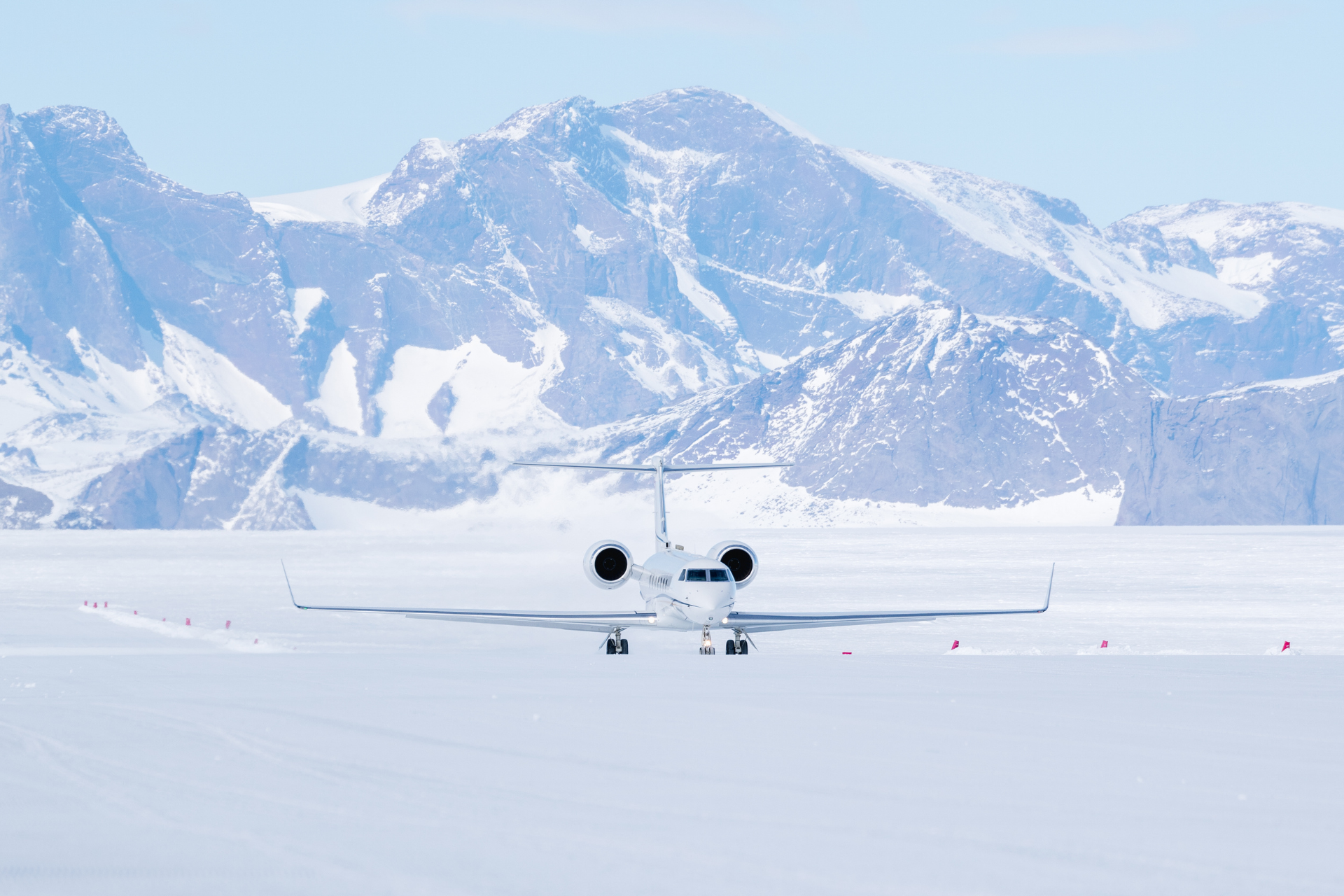 Private jet landing on a remote ice runway in Antarctica with snow-covered mountains behind