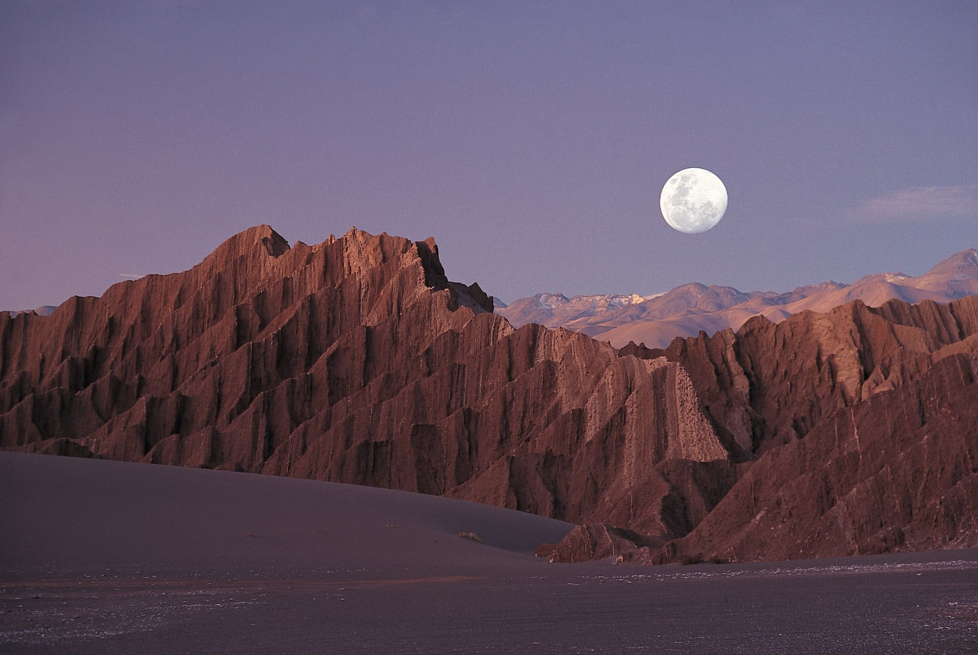 Moon rising over rugged Atacama Desert rock formations with distant Andes mountains at dusk in northern Chile