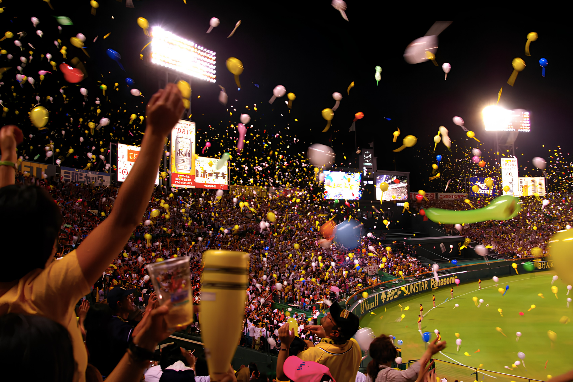 Night-time baseball game in Japan with fans celebrating in a brightly lit stadium as balloons fill the air