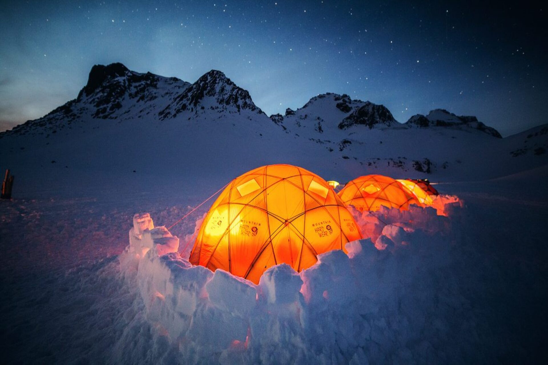 Illuminated glass dome tents in a snowy Arctic mountain landscape under a clear night sky