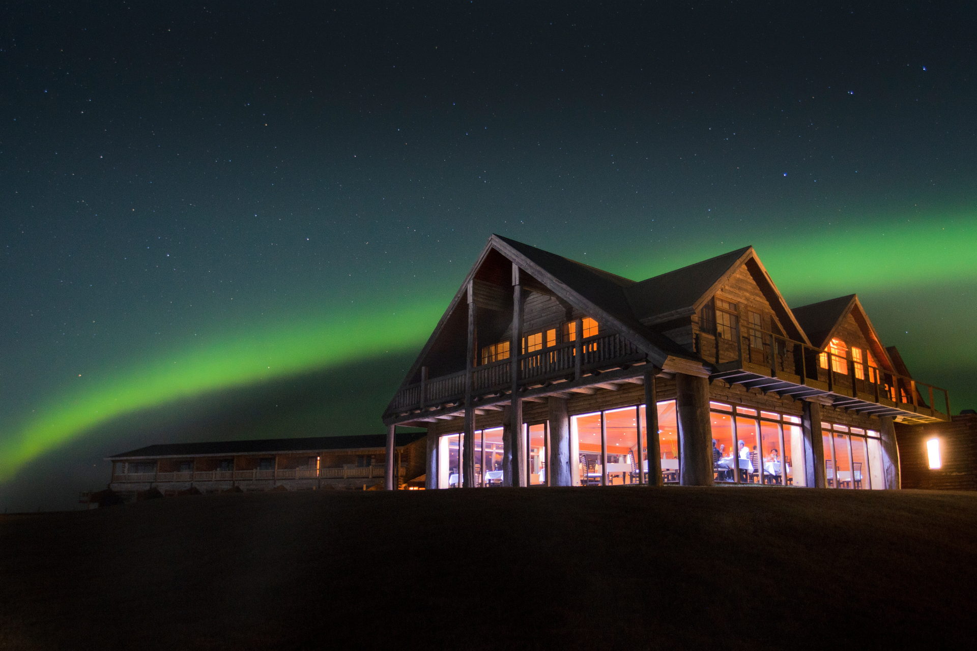 Northern lights glowing above a luxury Arctic lodge with warm interior lighting under a star-filled night sky