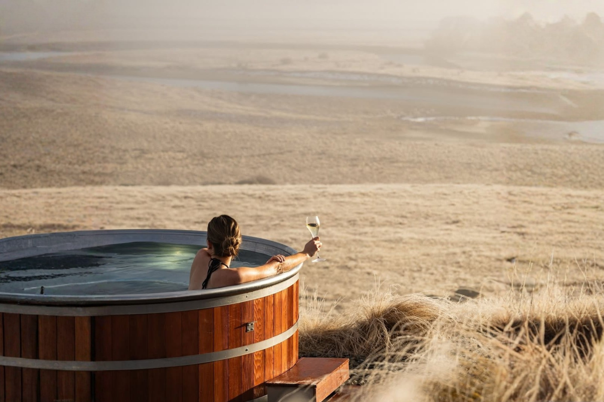 Outdoor hot tub overlooking a vast desert landscape with a glass of wine, showcasing remote luxury travel and unique dining escapes