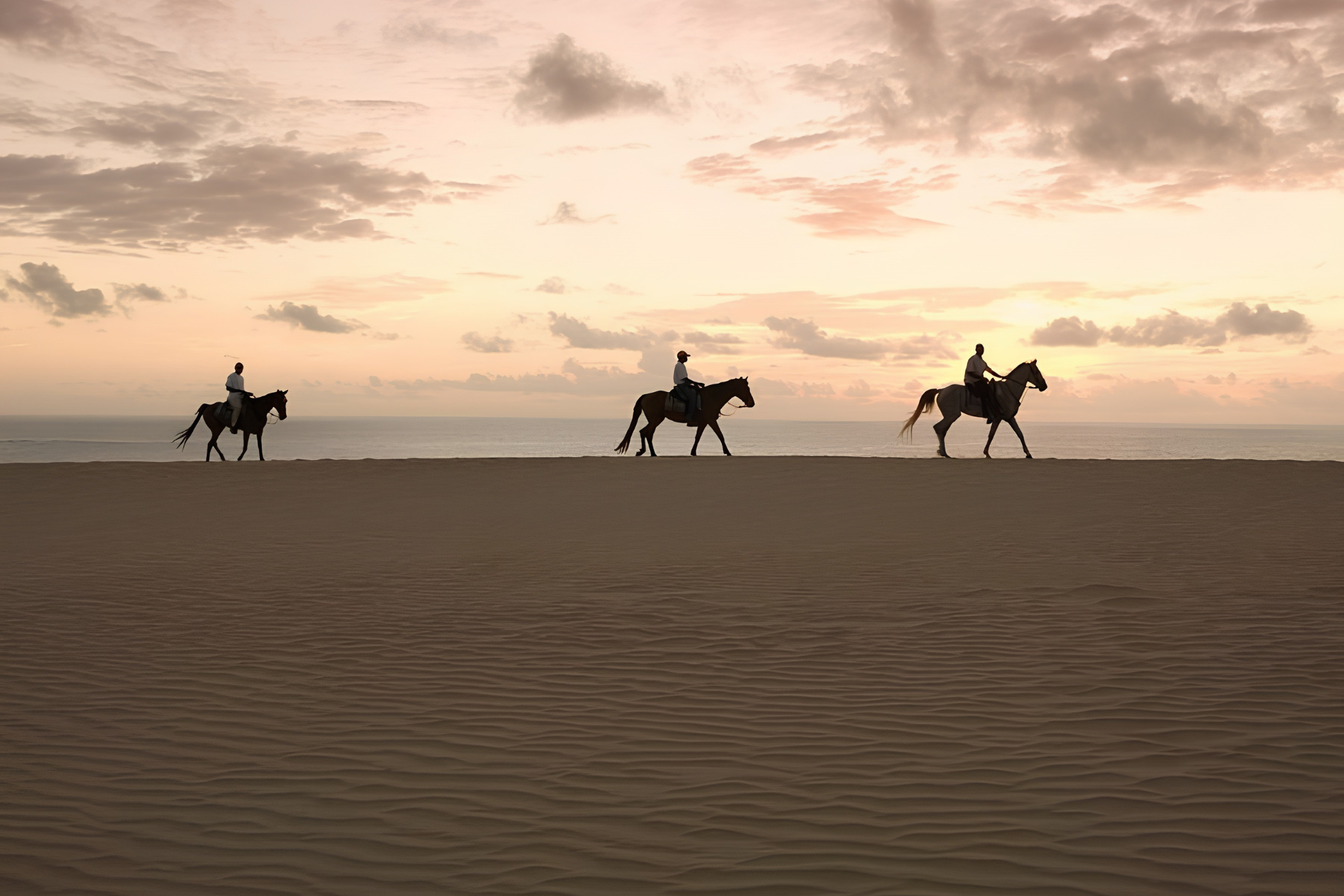 Travelers horseback riding across the sand dunes along Mozambique’s Indian Ocean coastline at sunset.
