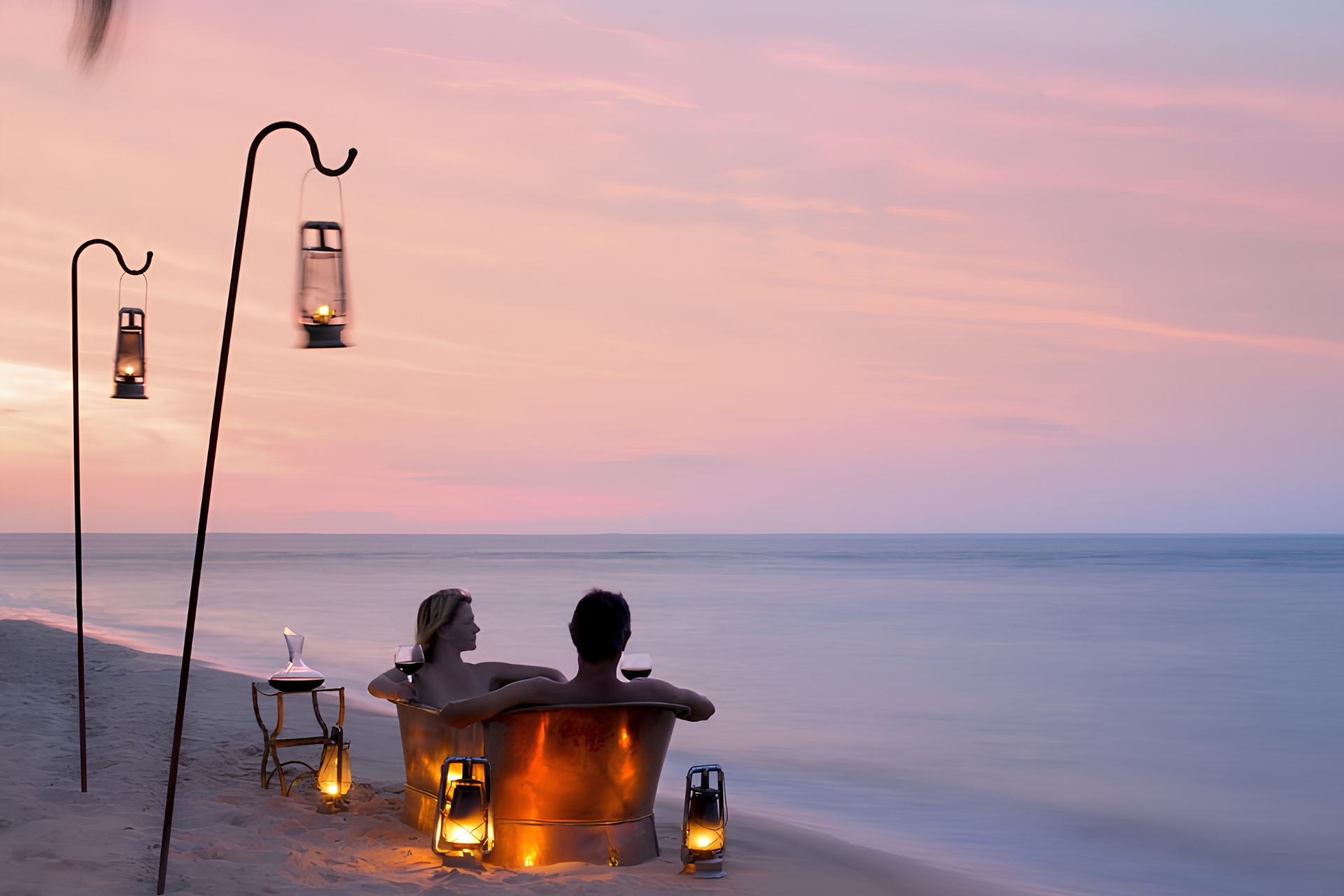 Couple enjoying a private alfresco copper bath with wine beside the Indian Ocean in Mozambique at sunset.