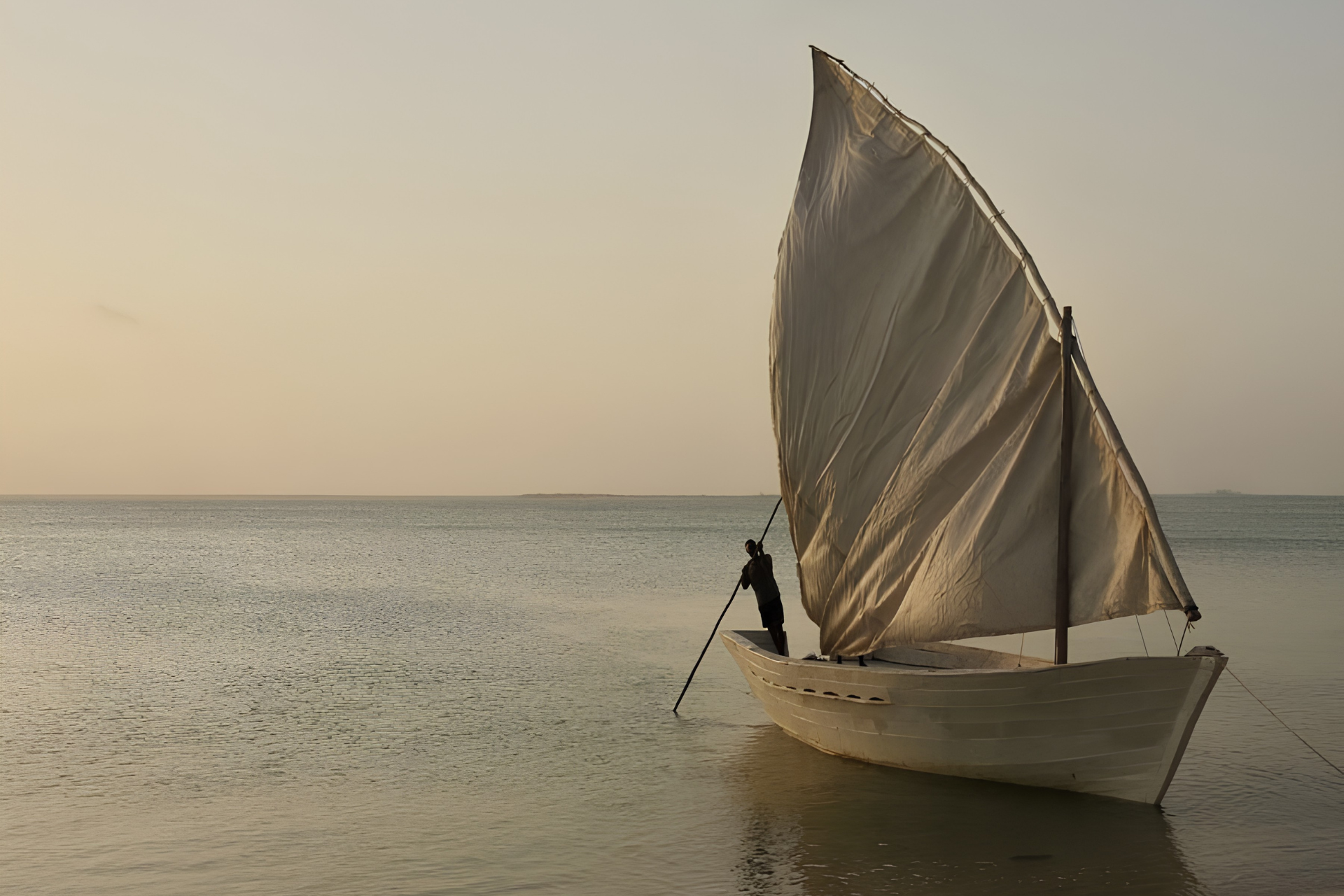 Traditional dhow sailing across the calm Indian Ocean off the coast of Mozambique at sunset.