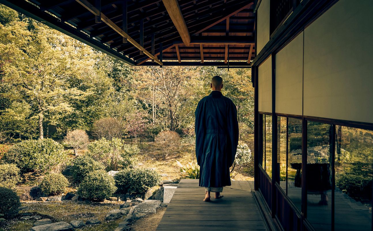 Buddhist monk walking barefoot along a temple veranda beside a Japanese garden