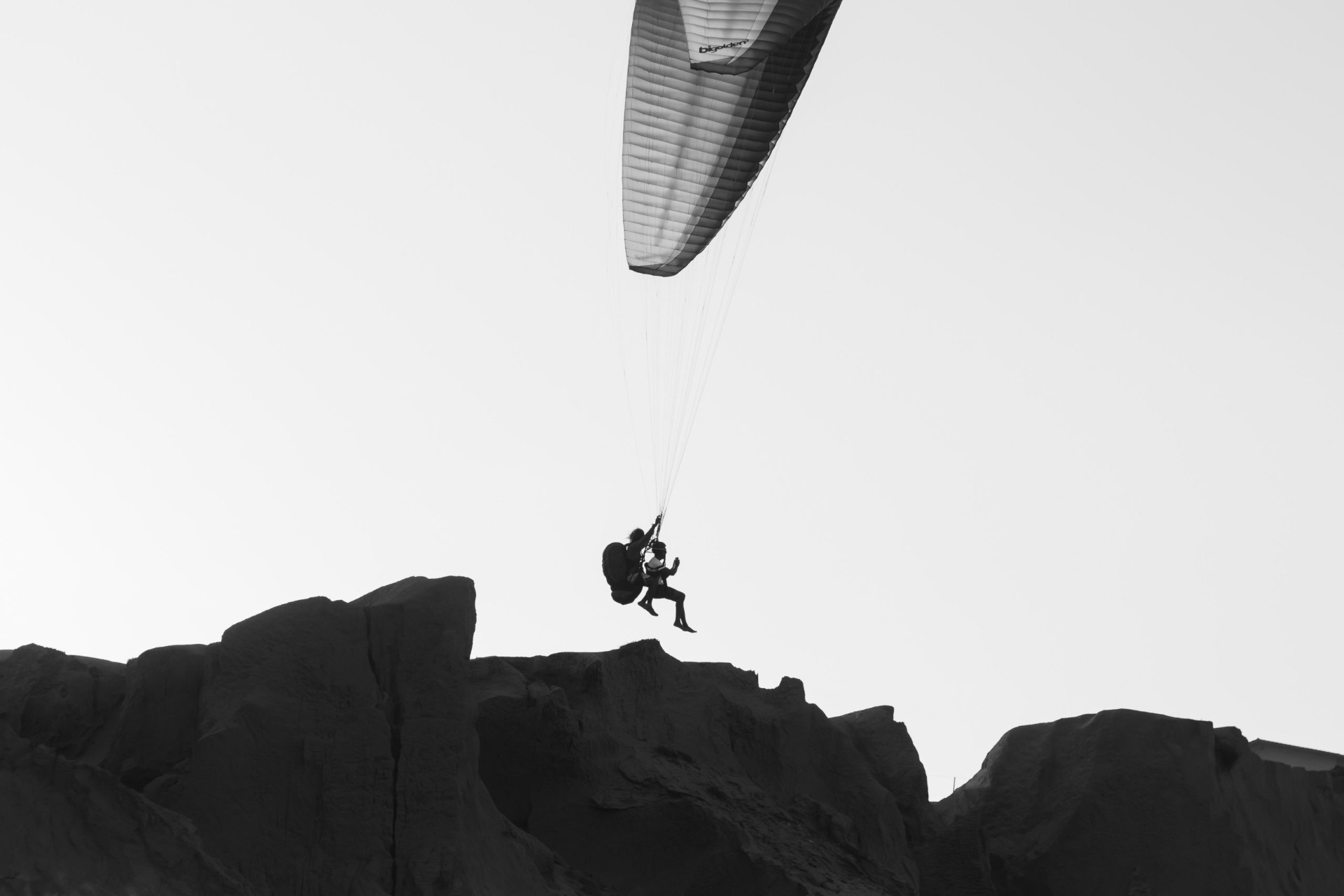 Paraglider flying over rugged mountain terrain