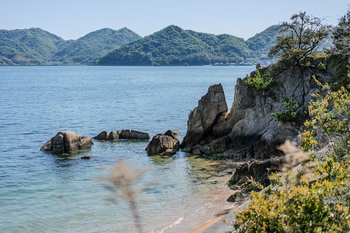 Rocky cove and calm blue water along the Seto Inland Sea, with forested islands across the channel