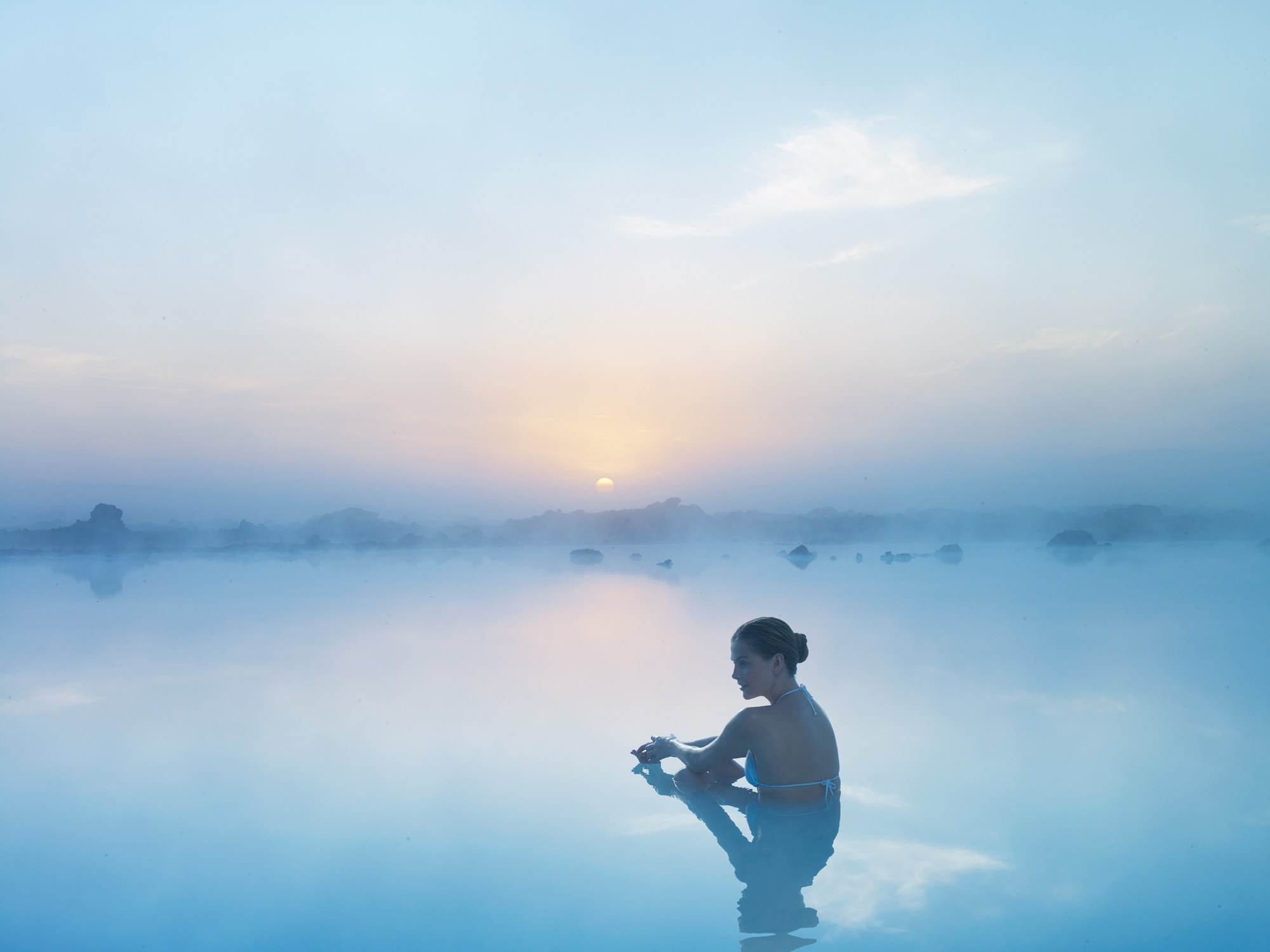 Woman relaxing in a steaming geothermal lagoon in Iceland at sunrise