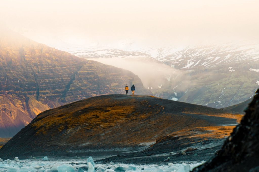 Two hikers on a ridge above a glacier lagoon in Iceland, with snow-capped mountains in the mist