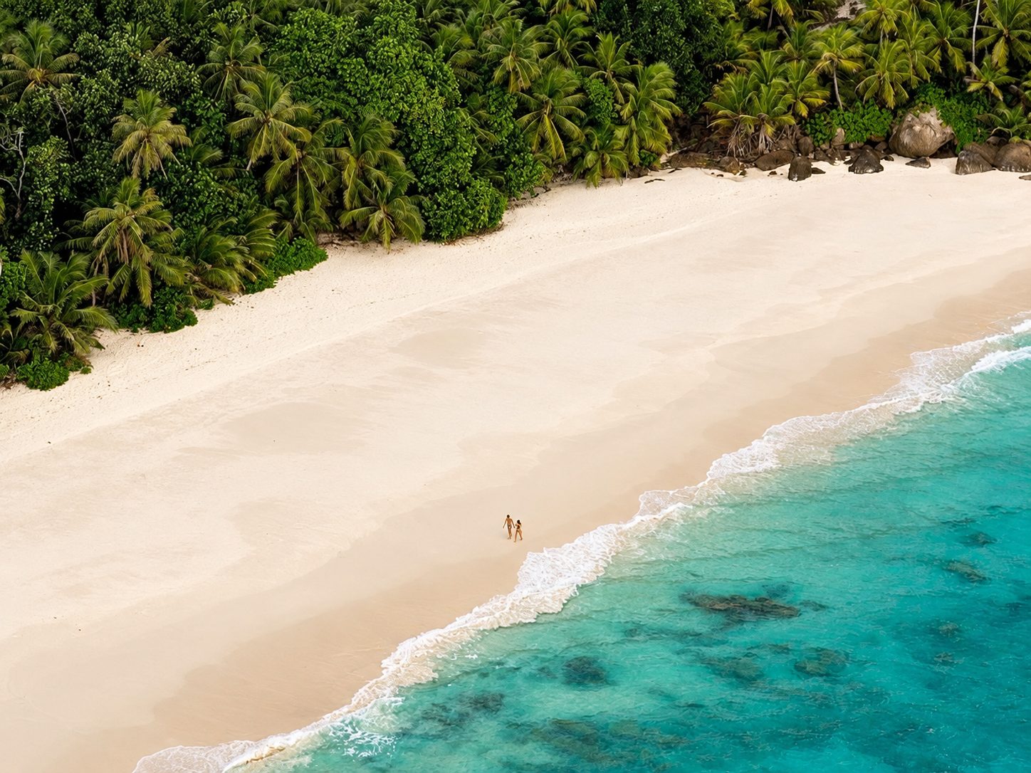Aerial view of a couple walking on a palm-lined white-sand beach in the Seychelles